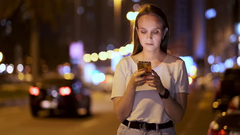 At-night-a-young-girl-sits-on-the-grass-in-a-big-city-and-looks-into-the-smartphone-screen-writes-a-message-and-maintains-her-personal-blog.